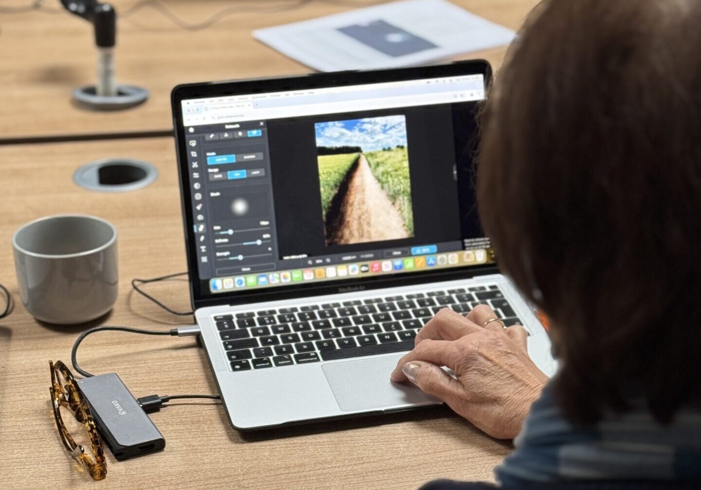Over-the-shoulder view of a woman editing an image in Pixlr, a web-based photo editing tool, on her laptop.