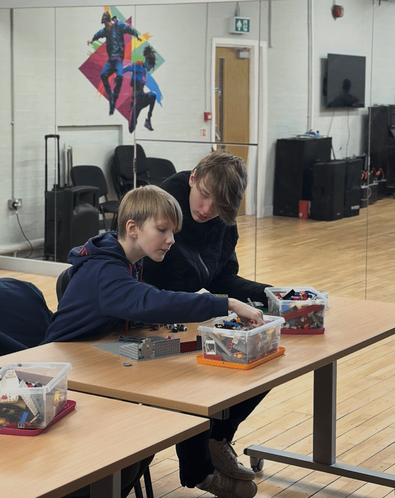 A classroom of adult students seated at laptops, with tutor Mariam at the front presenting photo editing information on a large screen.